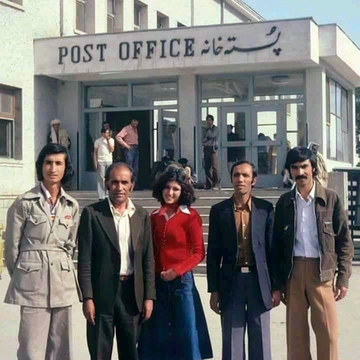 "Group of people in Kabul, including a woman in traditional Afghan attire, in front of a post office during the late 1970s or early 1980s.